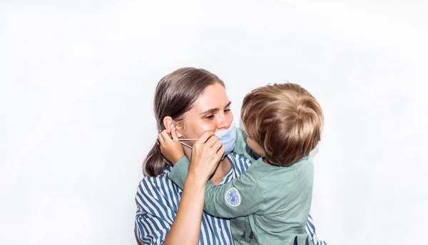 Fiatal nő, kék csíkos ingben, orvosi maszkban, egy babával a karjában. coronavirus elleni gyógyszer, covid 19, — Stock Fotó