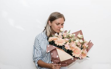 Çizgili mavi bluzlu genç kadın kocaman bir buket turuncu Gerbera gül çiçeği tutuyor. Kadına doğum günü hediyesi. 