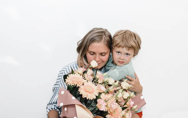 Filho e jovem mãe abraçar e beijar. a criança parabenizou sua mãe por seu aniversário e apresentou buquê — Fotografia de Stock