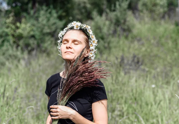 Mujer joven con una corona de margaritas en la cabeza al sol en un campo de hierba — Foto de Stock