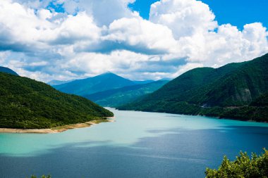 Berrak bir gökyüzü ve dağ tepelerinin arka planında mavi turkuaz berrak su ile dağ gölü
