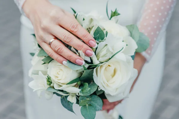 Main de mariée avec une élégante bague de mariage avec diamants en or blanc sur un bouquet de leurs pivoines — Photo