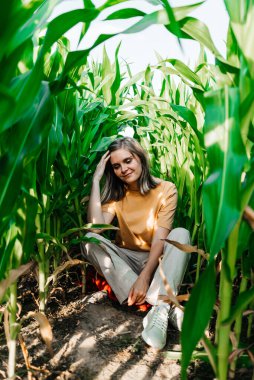 Sarı tişörtlü, mısır tarlasında kısa saçlı genç bir kadın.