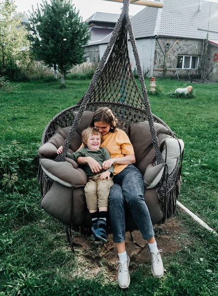 Mère et enfant montent sur une balançoire en rotin d'osier. fils secoue une femme, secoue des vacances d'été dans la nature — Photo