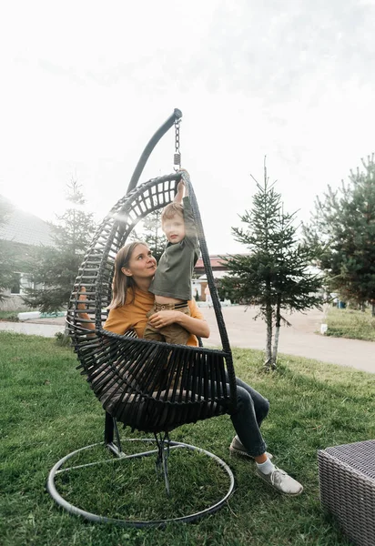 mother and child ride on a wicker rattan cocoon swing. son shakes a woman, shakes a summer vacation in nature