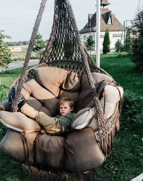 the child rides on a wicker rattan cocoon swing. son is swinging summer outdoor recreation