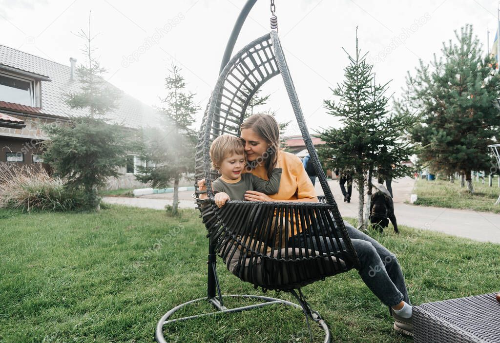 mother and child ride on a wicker rattan cocoon swing. son shakes a woman, shakes a summer vacation in nature