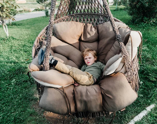 the child rides on a wicker rattan cocoon swing. son is swinging summer outdoor recreation