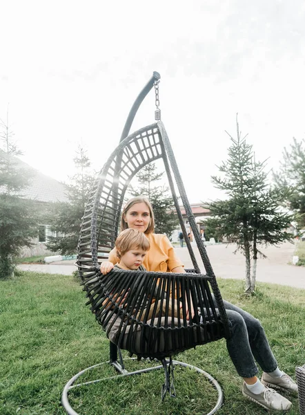 Mère et enfant montent sur une balançoire en rotin d'osier. fils secoue une femme, secoue des vacances d'été dans la nature — Photo