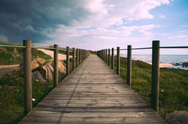  Gök gürültülü fırtınadan önce, kara bulutların altında, deniz kıyısında ahşap yol. Sahilde ve sahil kenarında tahta platform var..