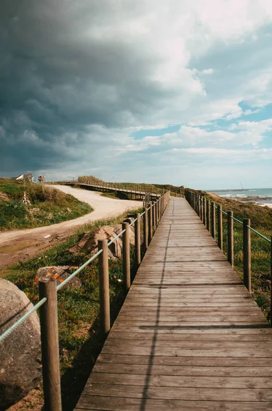 Wooden walkway at the seaside under dark clouds, before thunderstorm sky.  boardwalk near the coastline and beach, wooden platform.