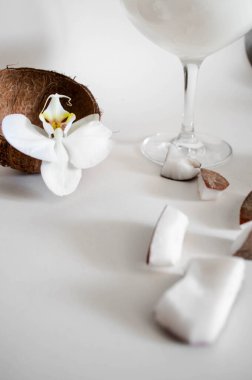 Beyaz arka planı olan bir bardakta hindistan cevizi kokteyli. Hindistan cevizi sütü, doğranmış hindistan cevizi. Sahne Olarak Çiçek Orkidesi