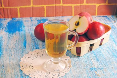 Bir bardak elma suyu ve ahşap arka planda kırmızı elmalar