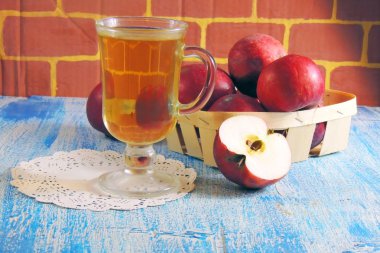 Bir bardak elma suyu ve ahşap arka planda kırmızı elmalar