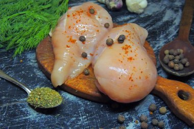 Tahta arka planda sarımsak, biber ve biberiyeli çiğ tavuk filetosu.