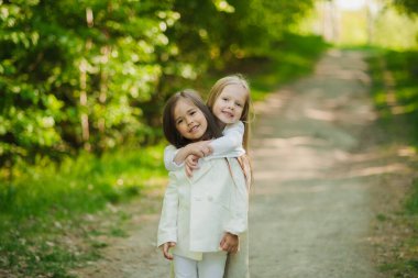 Parkta beyazlar içinde sarılan küçük kızlar. Yazın iki küçük kız parkta oynuyor. Arkadaşlık..