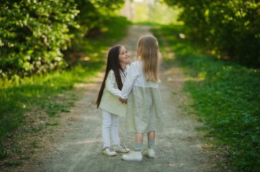 Beyaz elbiseli küçük kızlar parkta el ele tutuşuyorlar. Yazın iki küçük kız parkta oynuyor. Arkadaşlık..