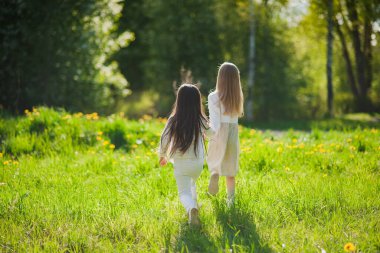Beyaz elbiseli küçük kızlar parkta el ele tutuşuyorlar. Yazın iki küçük kız parkta oynuyor. Arkadaşlık..