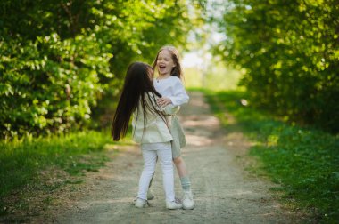 Beyaz elbiseli küçük kızlar el ele tutuşup parka atlıyorlar. Yazın, iki küçük kız parkta oynuyor. Arkadaşlık..