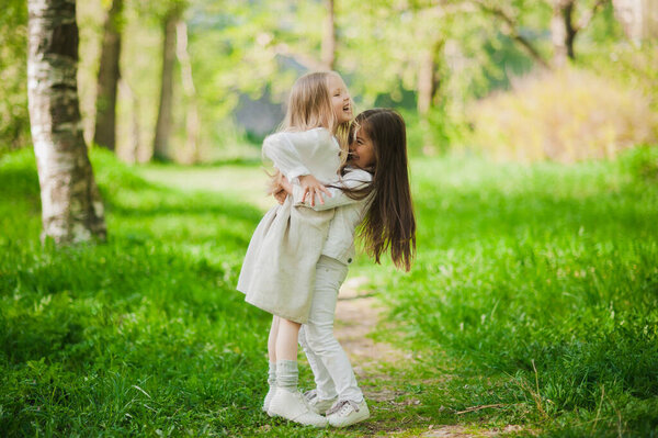 Little girls in white hold hands in the Park. Two little girls play in the Park in the summer. Friendship.