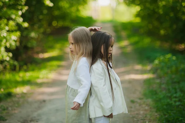 Beyaz elbiseli küçük kızlar el ele tutuşup parka atlıyorlar. Yazın, iki küçük kız parkta oynuyor. Arkadaşlık..