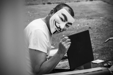 Paris - Fransa - 19 Mayıs 2018 - adam portresi ile kan davası maskesi ve vintage koltuk üzerinde terkedilmiş fabrikada coumputer. Bu maske online hacktivist grubu Anonymous için iyi bilinen bir semboldür