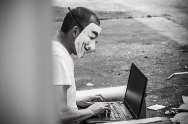 Paris - Fransa - 19 Mayıs 2018 - adam portresi ile kan davası maskesi ve vintage koltuk üzerinde terkedilmiş fabrikada coumputer. Bu maske online hacktivist grubu Anonymous için iyi bilinen bir semboldür