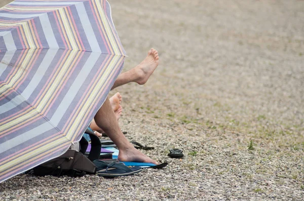 Nahaufnahme Von Füßen Die Einem Kieselstrand Aus Einem Sonnenschirm Herausragen — Stockfoto