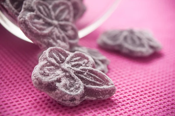 Zbliżenie Tradycyjnych Fioletowe Cukierki Kształcie Kwiatów Spadają Szklanym Pojemniku Różowym — Zdjęcie stockowe