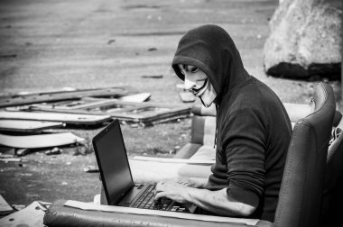 Paris - Fransa - 19 Mayıs 2018 - adam portresi ile kan davası maskesi ve vintage koltuk üzerinde terkedilmiş fabrikada coumputer. Bu maske online hacktivist grubu Anonymous için iyi bilinen bir semboldür