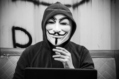 Paris - Fransa - 19 Mayıs 2018 - adam portresi ile kan davası maskesi ve vintage koltuk üzerinde terkedilmiş fabrikada coumputer. Bu maske online hacktivist grubu Anonymous için iyi bilinen bir semboldür