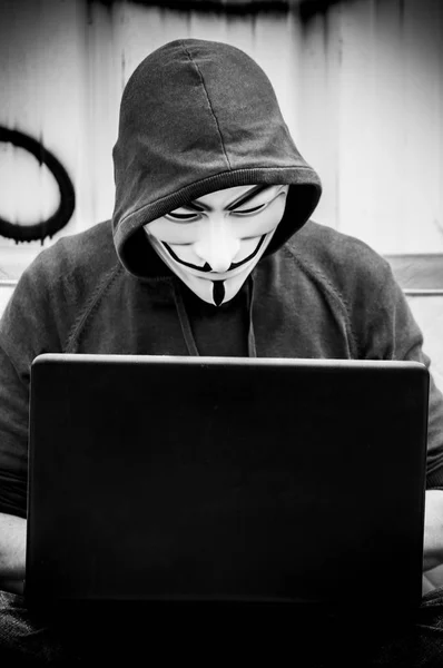 2018年5月19日 在老式扶手椅上的废弃工厂里 用仇恨面具和 Coumputer 的人画像 这个面具是一个知名的符号为在线黑客组匿名 — 图库照片