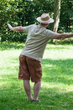 Arkadan görünüm kentsel Park'ta tai chi yapma şapkalı yaşlı adam portresi 