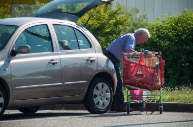 Mulhouse - Fransa - 21 Haziran 2018 - yaşlı adam arabasında onun paketleri depolama otopark süpermarket arabası ile yürürken