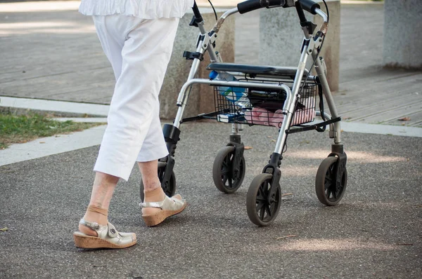 closeup of old woman walking with walker assistance in urban park