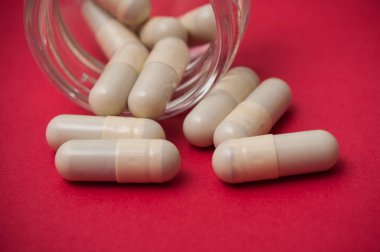 Şeffaf konteyner kırmızı zemin üzerine düşen hapları closeup