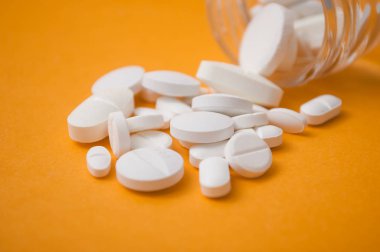 Cam kapsayıcıdan turuncu zemin üzerine düşen beyaz pils closeup