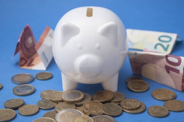 Euro banka banknot ve madeni paraların çevresinde mavi zemin üzerine beyaz bir kumbara closeup