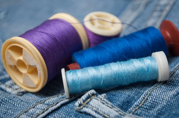 Closeup of sewing thread spool bobbin on blue jeans background — Stock Photo, Image