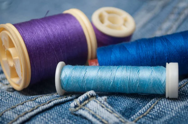 Closeup of sewing thread spool bobbin on blue jeans background — Stock Photo, Image