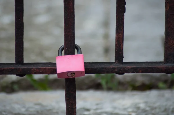 Closeup of pink padlock  on metallic grid in the city — Stock Photo, Image