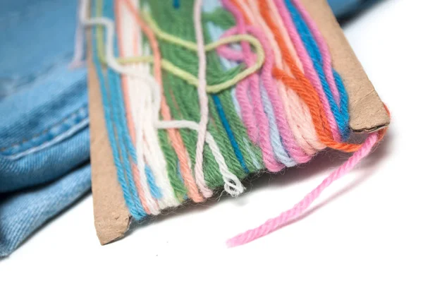 Closeup of colorful woolen threads on white table on blue jeans — Stock Photo, Image