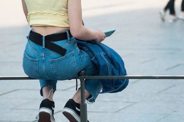 Nahaufnahme eines Mädchens, das auf einem Metallzaun sitzt und blaue Jeans trägt — Stockfoto