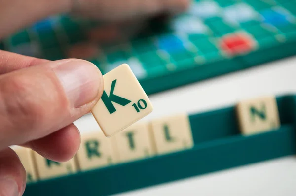 Close-up van plastic letters K in de hand op Scrabble bordspel — Stockfoto