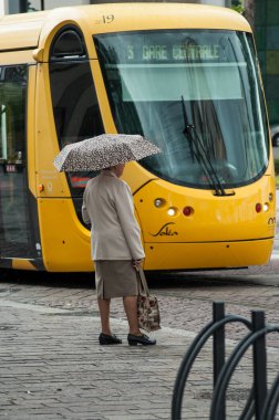 tramvay istasyonu önünde şemsiye ile sokakta duran yaşlı kadın