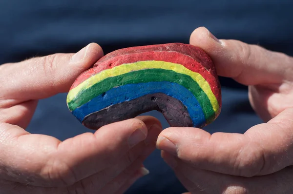 Primer plano de la pintura del arco iris en guijarro de piedra en la mano — Foto de Stock