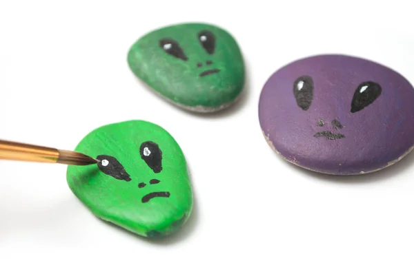 closeup of aliens painting on stone pebbles on white background