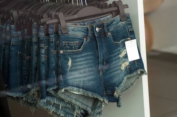 Pantalones vaqueros rotos cortos en perchas en una tienda de moda — Foto de Stock
