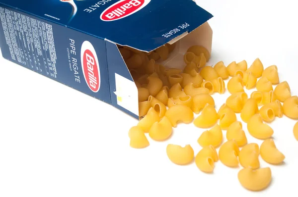 Närbild av pipe Rigate pasta faller från Barilla pappkartong på vit bakgrund, det berömda märket av italiensk pasta — Stockfoto