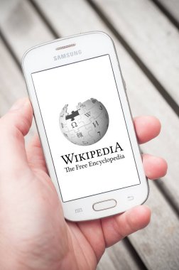 Closeup of Wikipedia logo on smartphone in hand in the street clipart